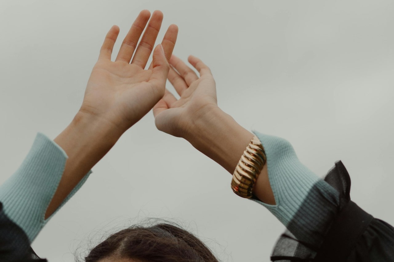 A person’s arms raised above their head, a chunky cuff bracelet on their left wrist.