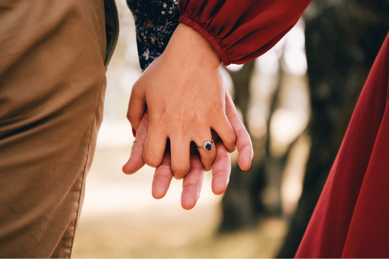 Close up of two people holding hands, one wearing a sapphire engagement ring