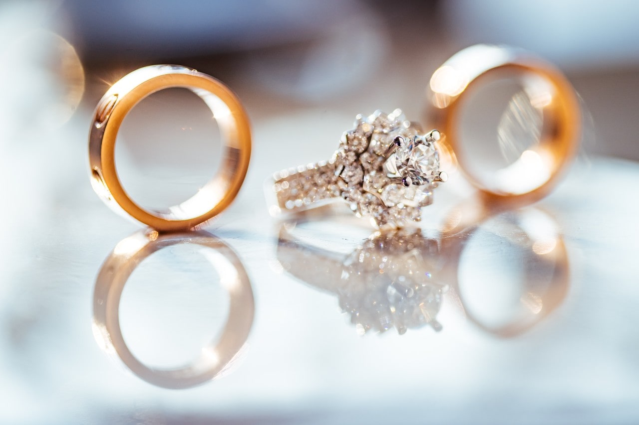 Three rings sitting on glass, one a diamond-studded engagement ring