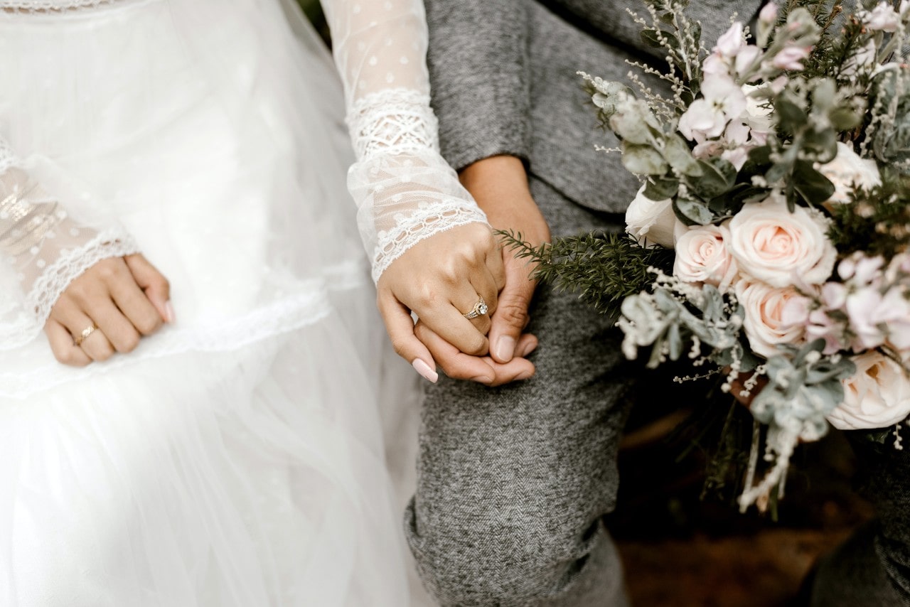 A bride and groom holding hands, the bride wearing a diamond engagement ring