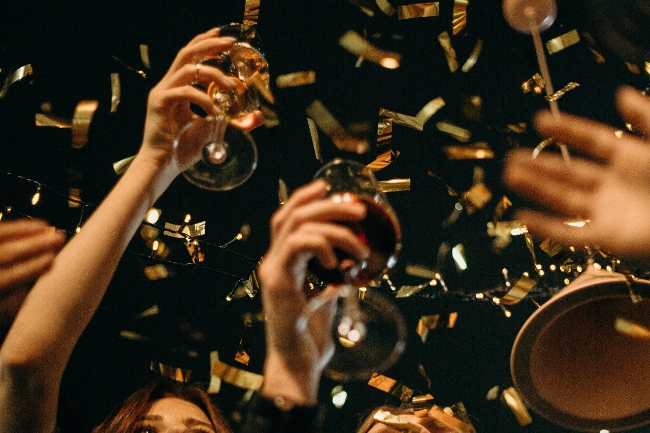 A group of adults raise their wine glasses to celebrate New Years’ Day as golden confetti rains down from the night sky