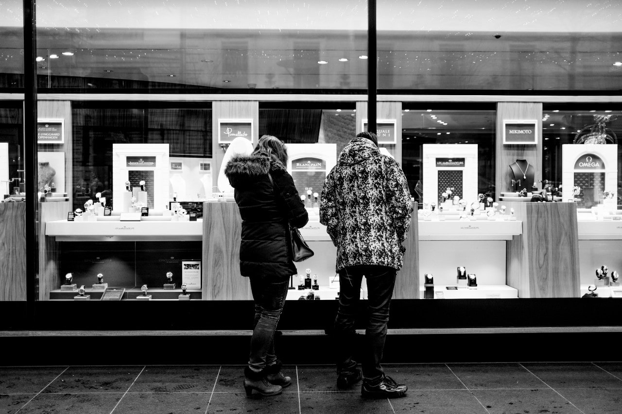 A couple window-shops from the outside of a closed jewelry store during the night