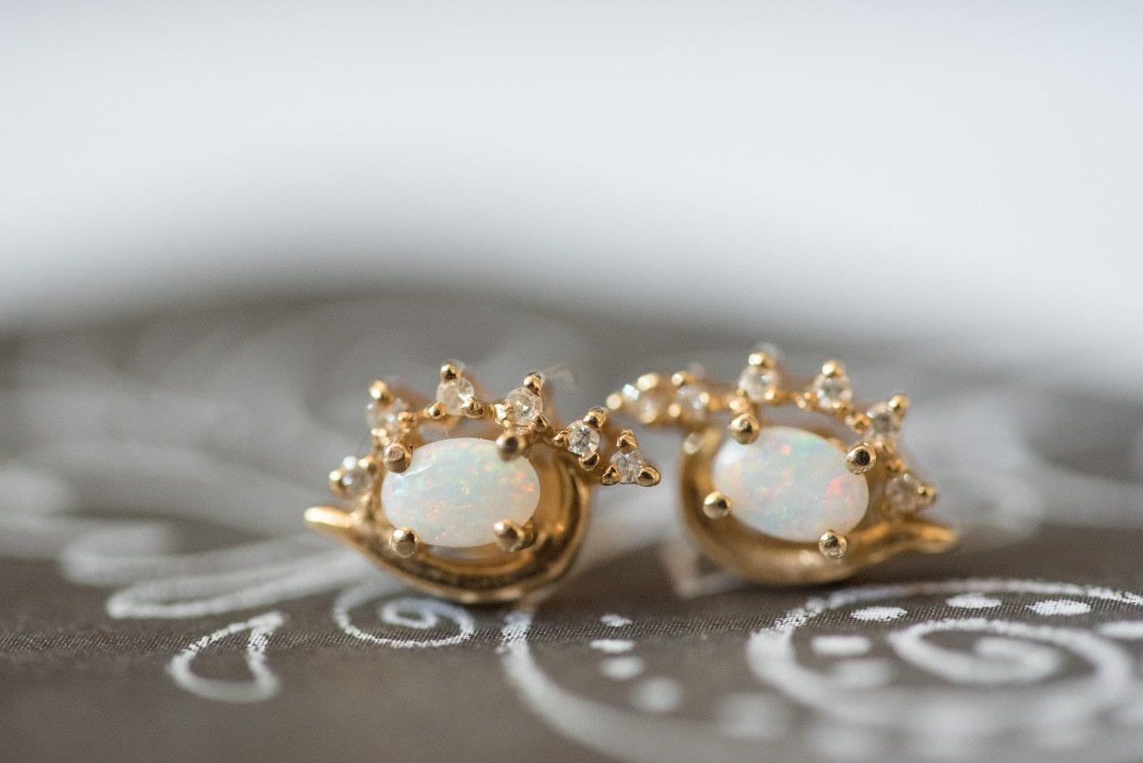 A close up of a pair of gold opal studs with diamond accents sitting on a patterned brown fabric