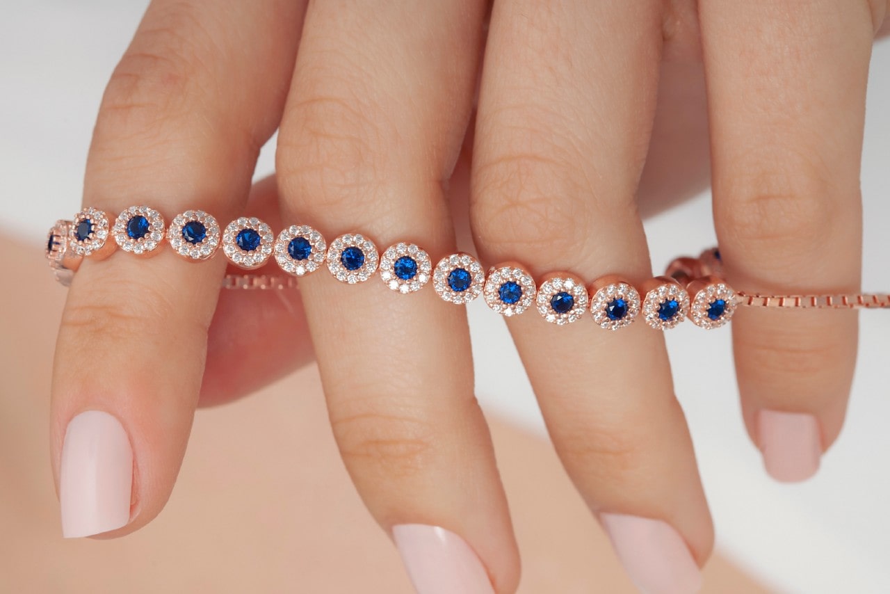 Close up image of a hand with manicured nails holding a sapphire and diamond bracelets wrought in rose gold