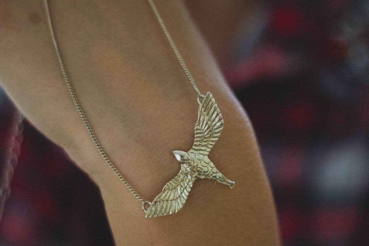 A hand holding a gold necklace featuring a large bird motif with sculpted details