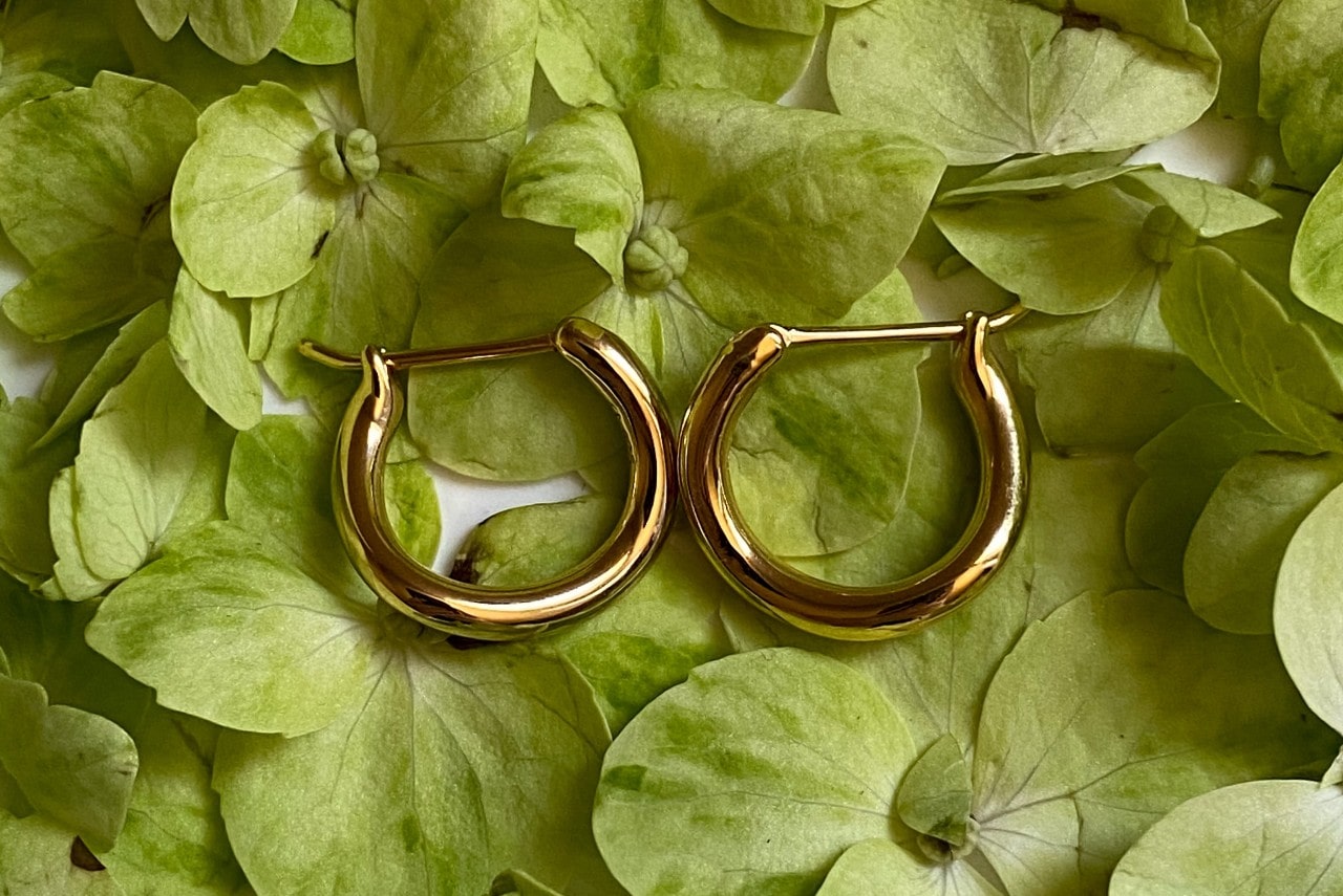 A pair of gold huggie earrings on a bed of green leaves