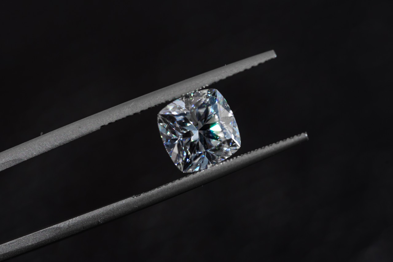 A jeweler displays a cushion-cut diamond against a black background for maximum elegance
