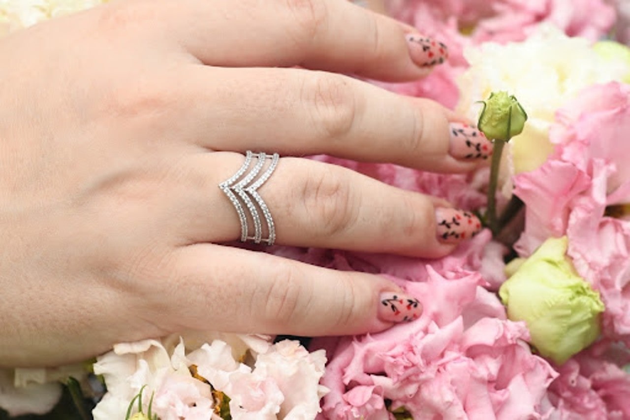 A woman with painted nails wears a fashion ring as she touches a bouquet of flowers