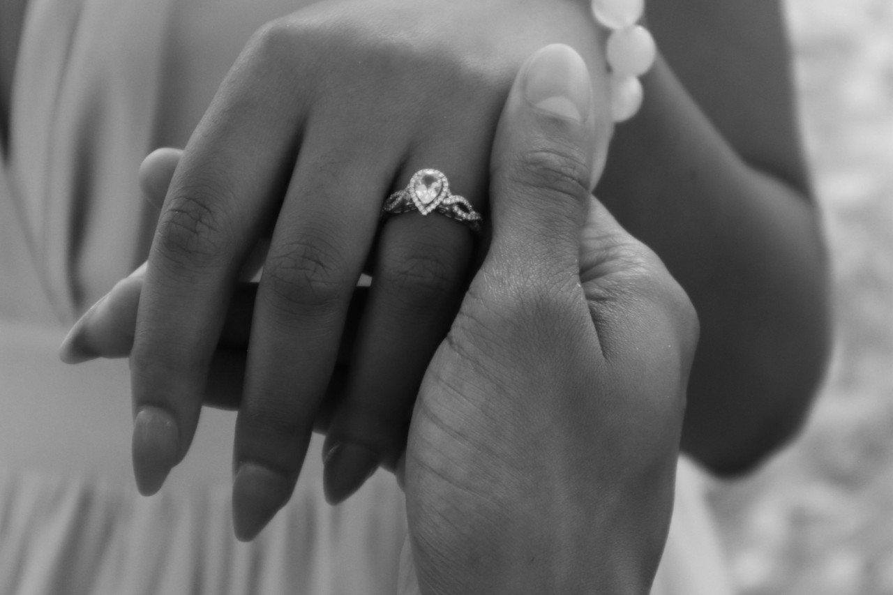 Black and white image of a groom holding his bride’s hand which is decorated with a marquise cut engagement ring