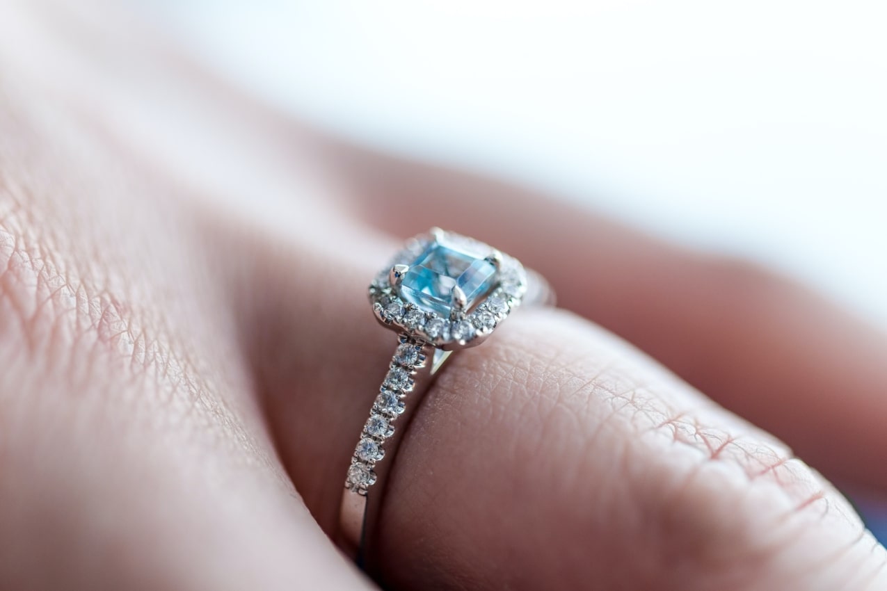Close up image of a princess cut engagement ring with a light blue center stone