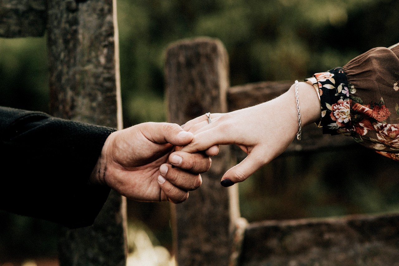 An engaged couple holds hands in front of a fence