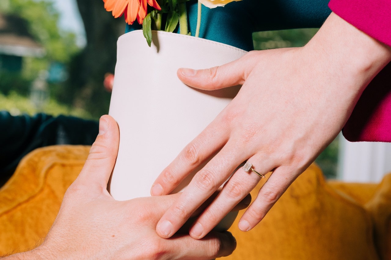 A couple passing a flower pot, the woman wearing a diamond engagement ring