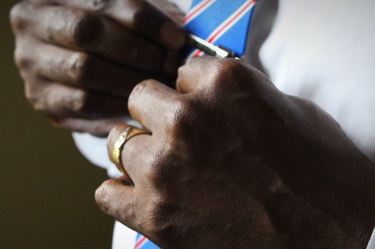 Fancy man straightening his tie clip with a gold band in clear view.