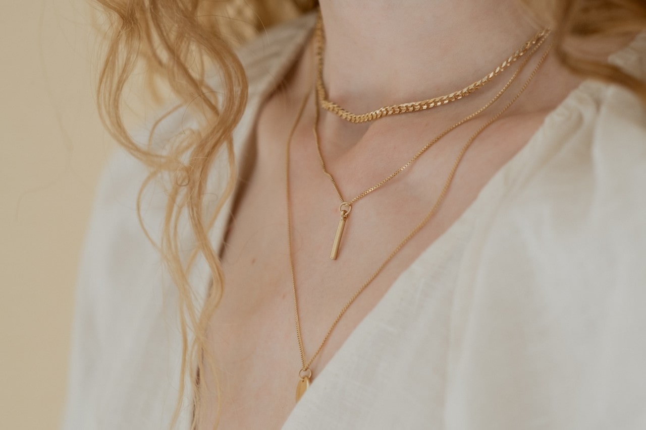 close up image of a woman’s neckline adorned in three gold necklaces of different lengths and styles