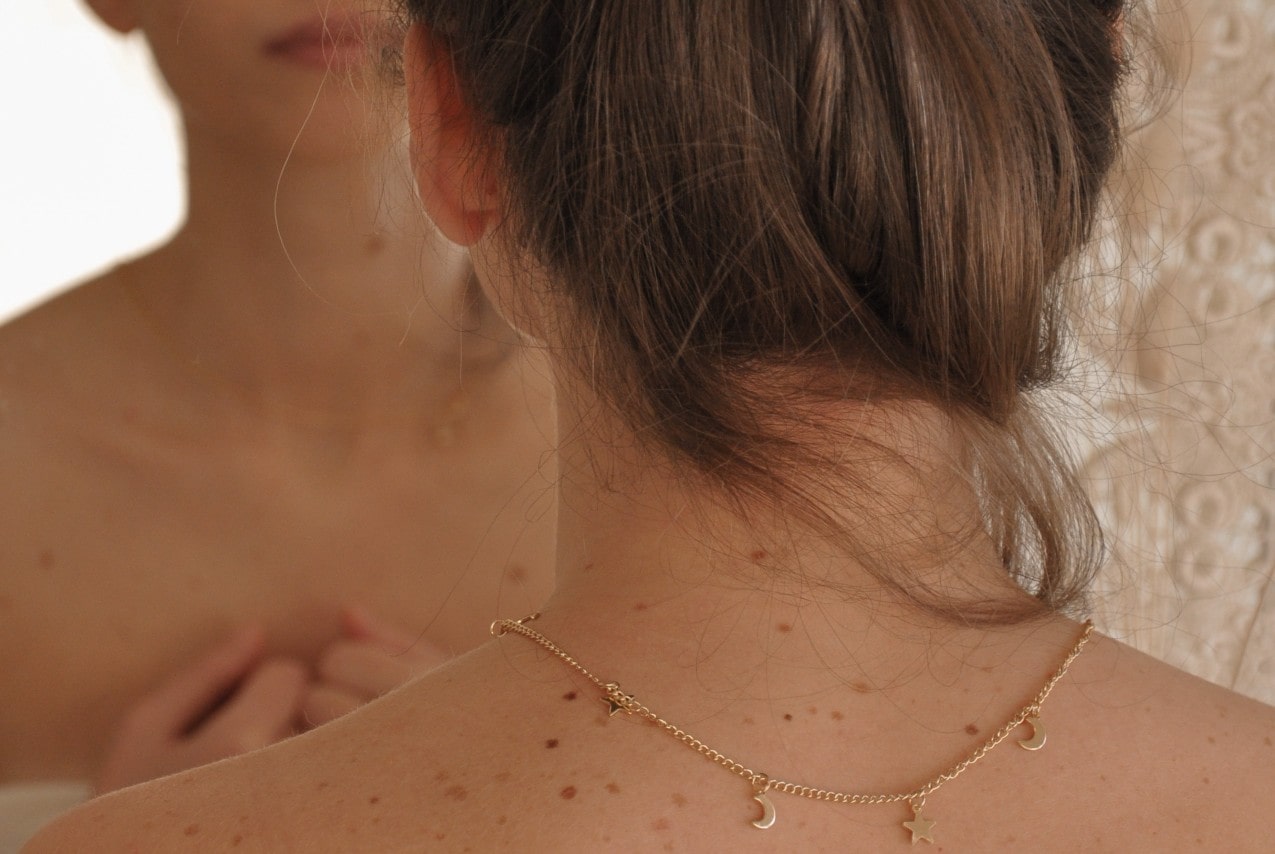 posterior view of a woman wearing a gold station necklace with celestial pendants