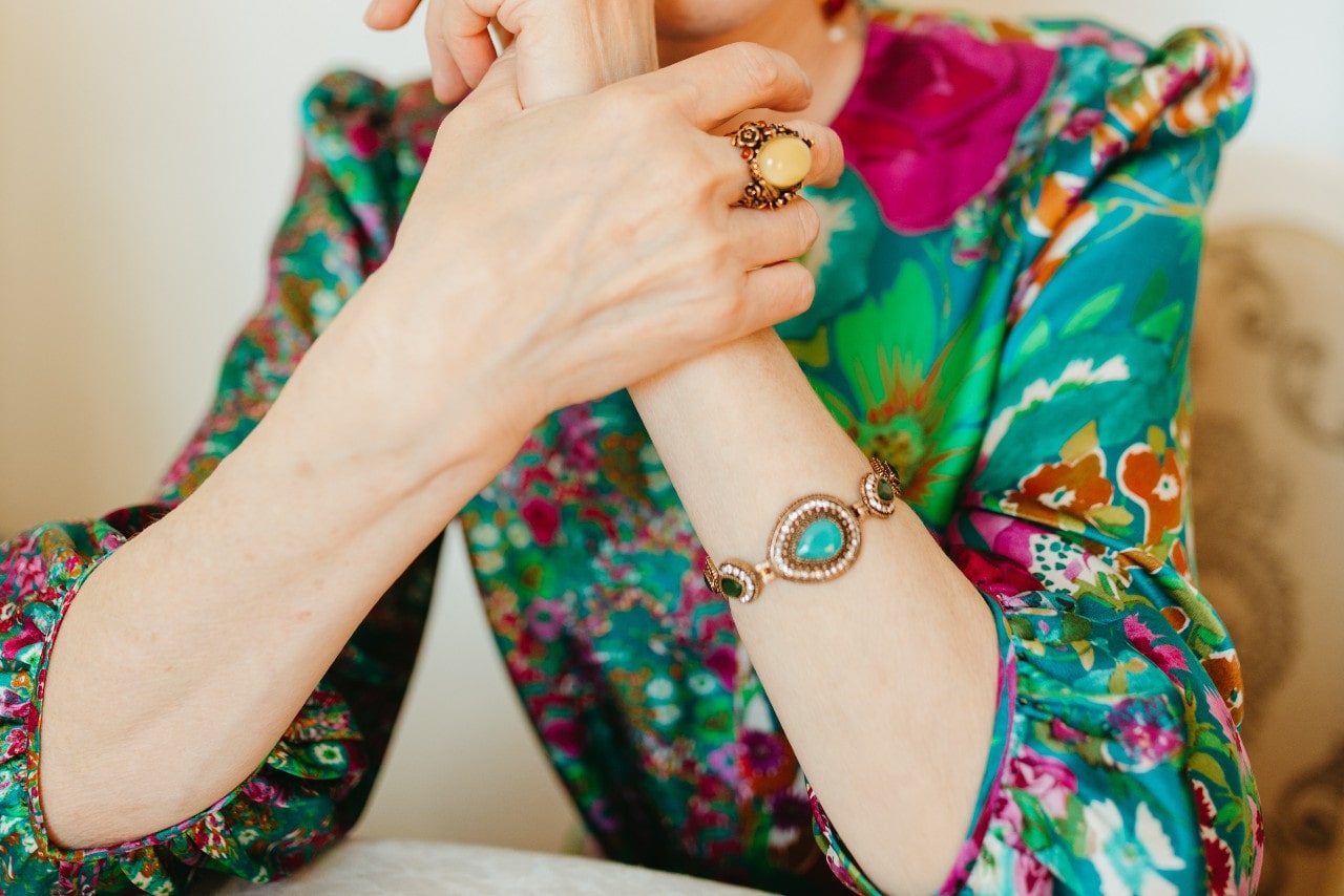 a woman wearing a colorful blouse and a gemstone bracelet and gemstone ring