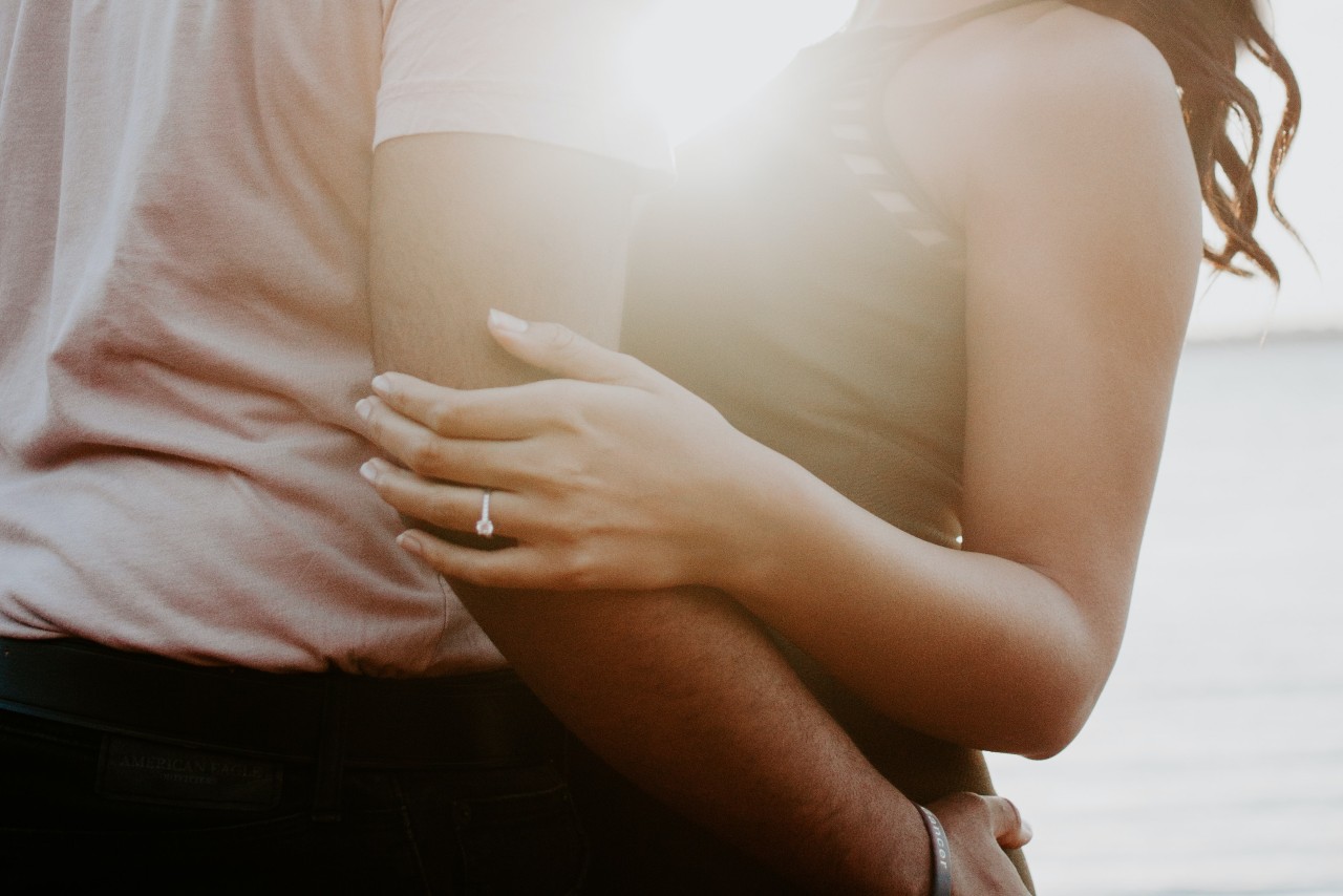 A couple embraces as the sun rises, the woman wearing an engagement ring