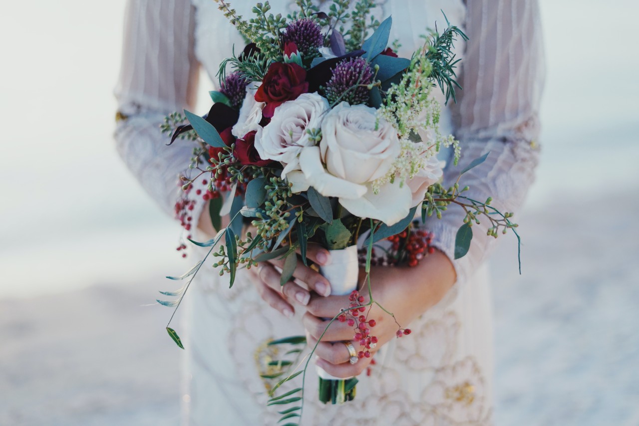A bride holds a bouquet, showing her engagement ring and wedding band