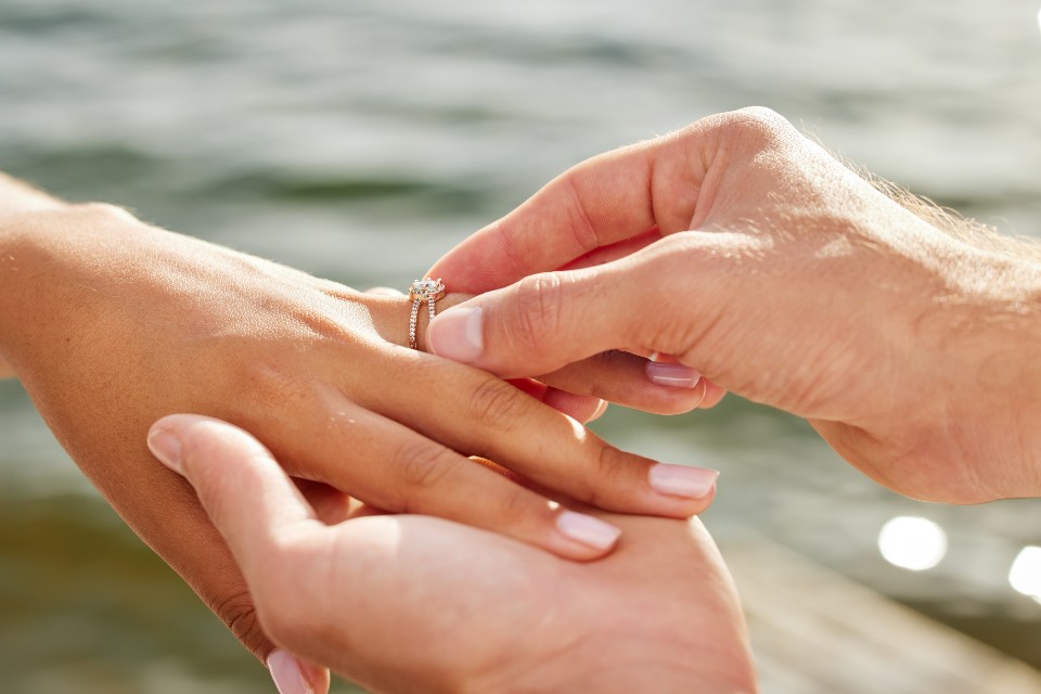 A close-up of a man slipping a delicate engagement ring onto his bride-to-be’s finger.