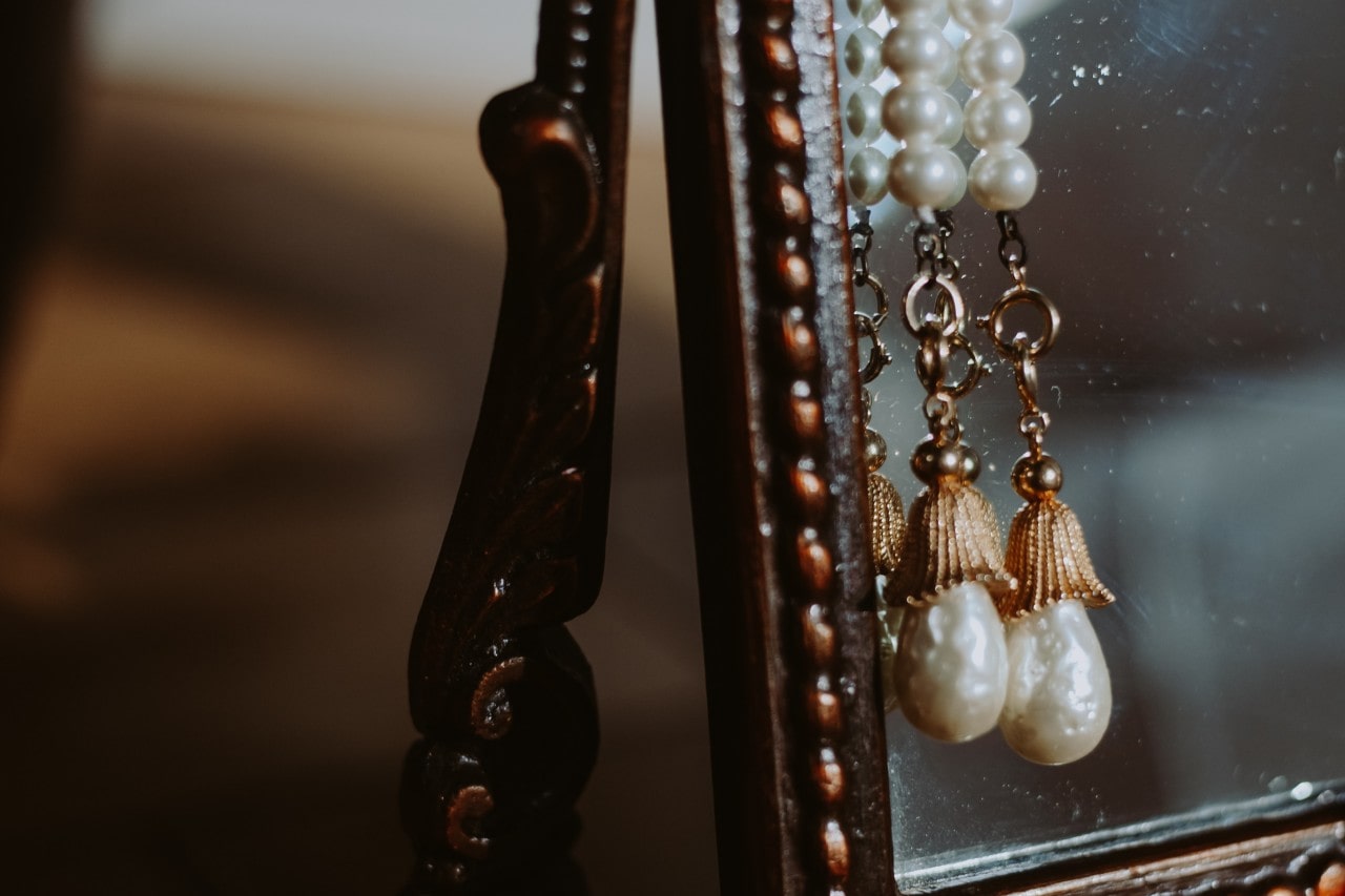 A pair of pearl drop earrings hang off a tabletop mirror.