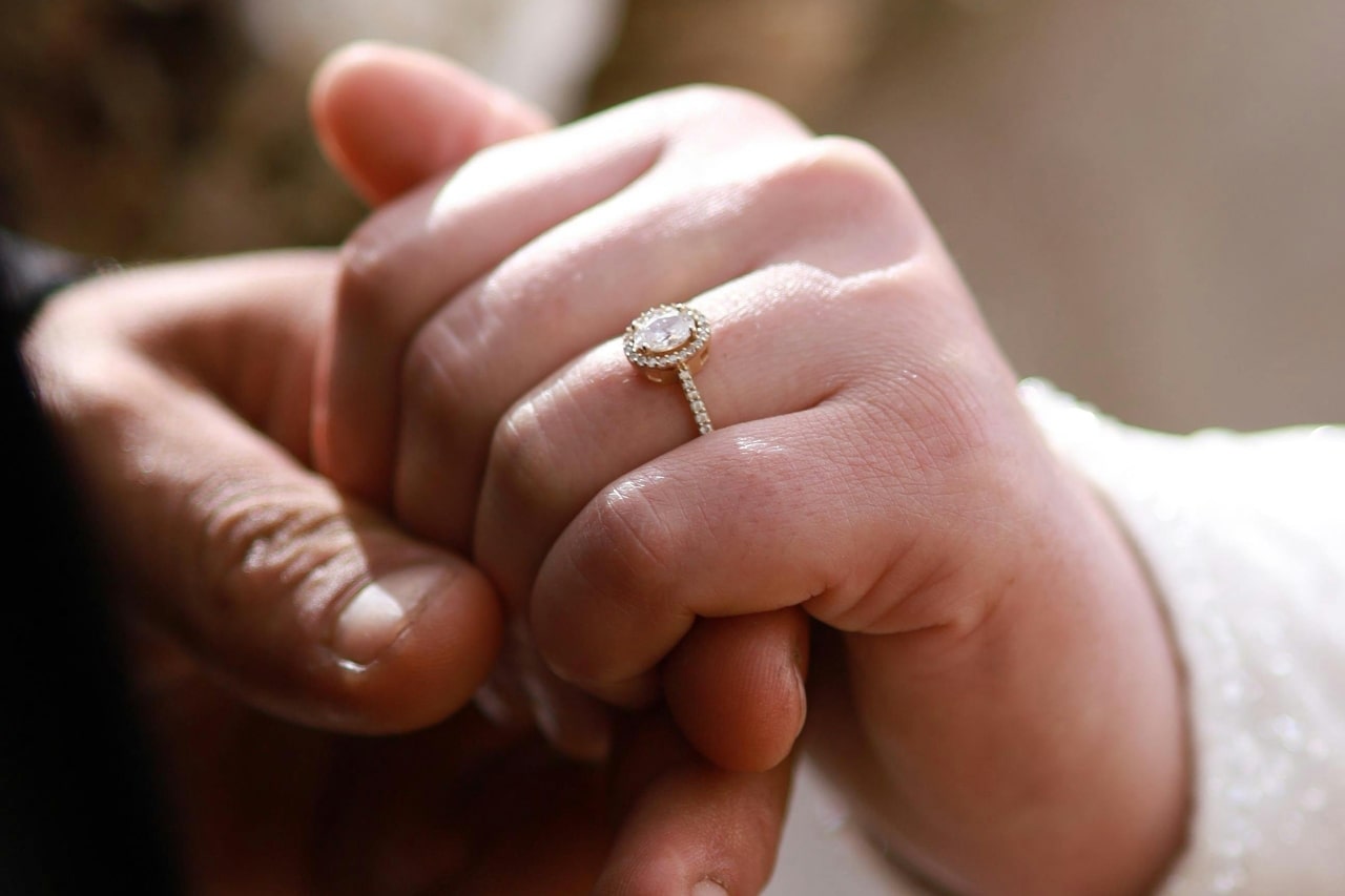 a man’s hand holding a woman’s that is adorned with a yellow gold diamond engagement ring