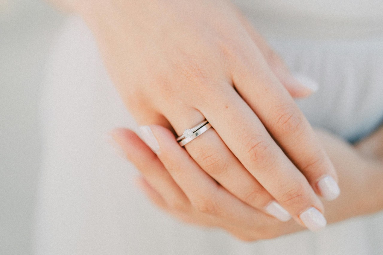 a woman’s hands, one of which is adorned in a simple wedding band and engagement ring