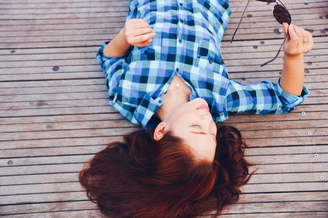 A young woman in a flannel shirt laying on a wooden deck.