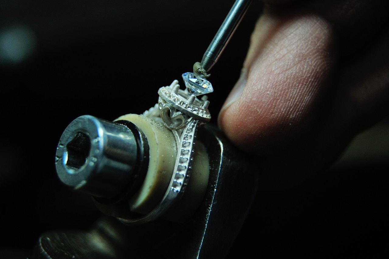 A jeweler sets a round-cut center diamond in a halo setting.