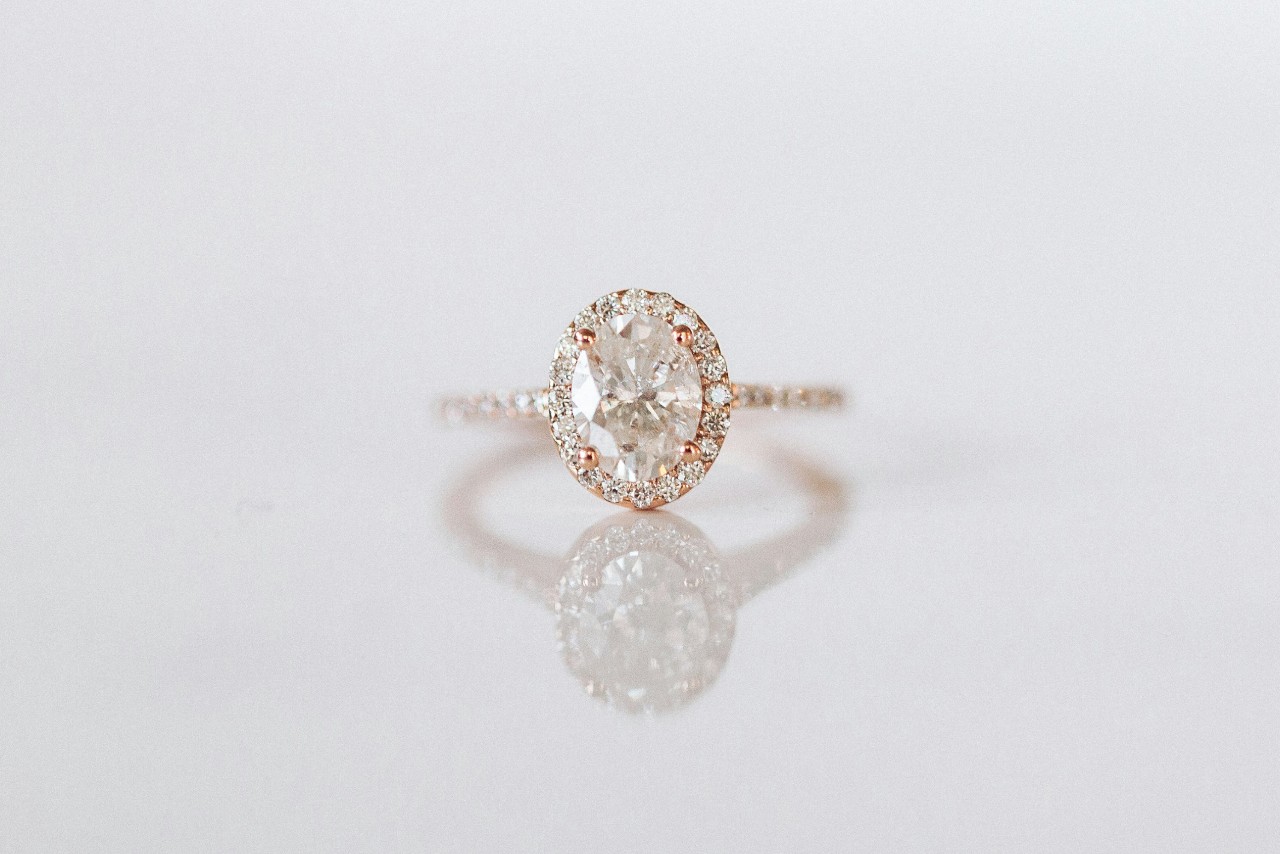 A wide view of a delicate yet stunning halo engagement ring with an oval center stone and side stone band.