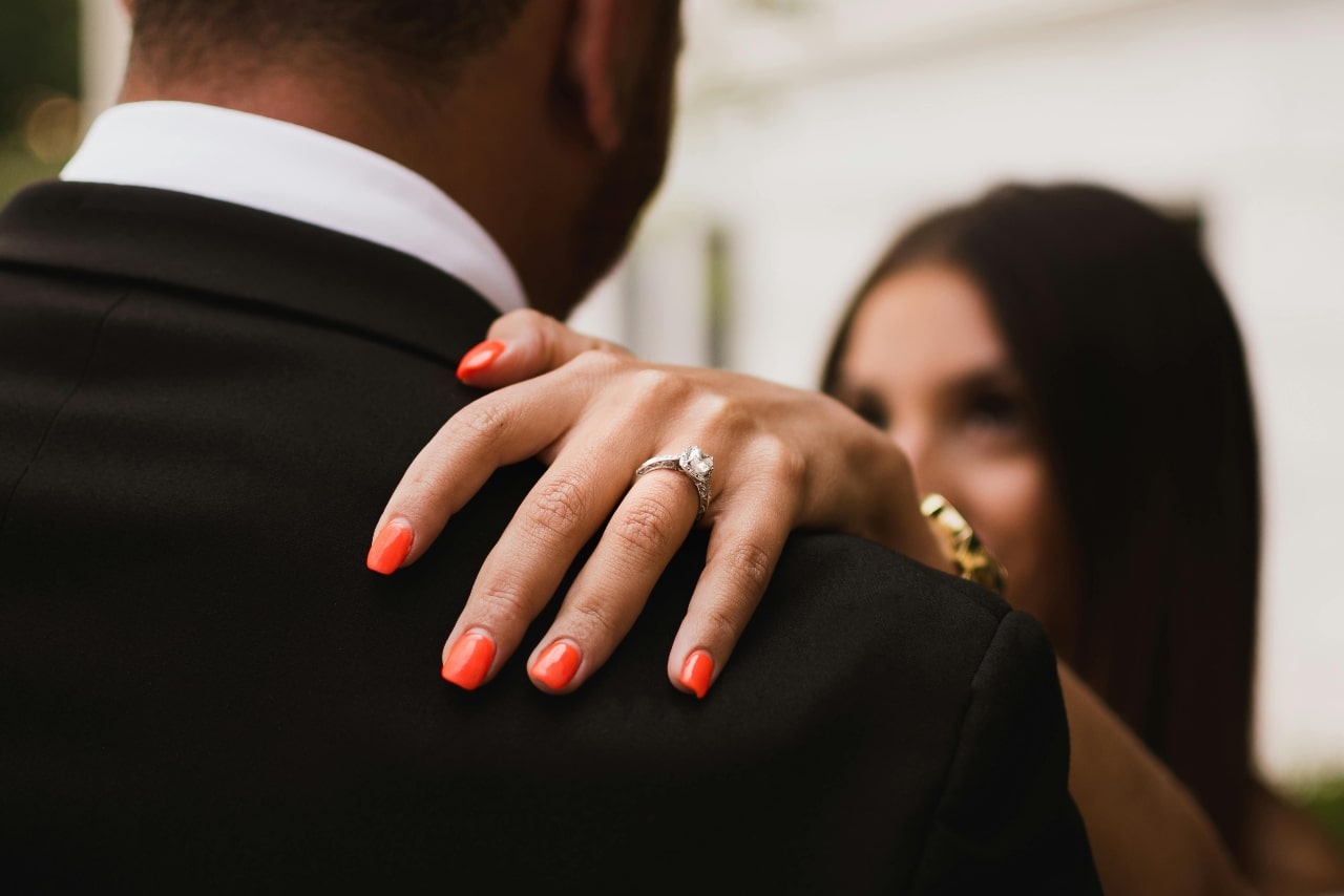 A woman resting her hand on a man’s shoulder, showing her side stone engagement ring