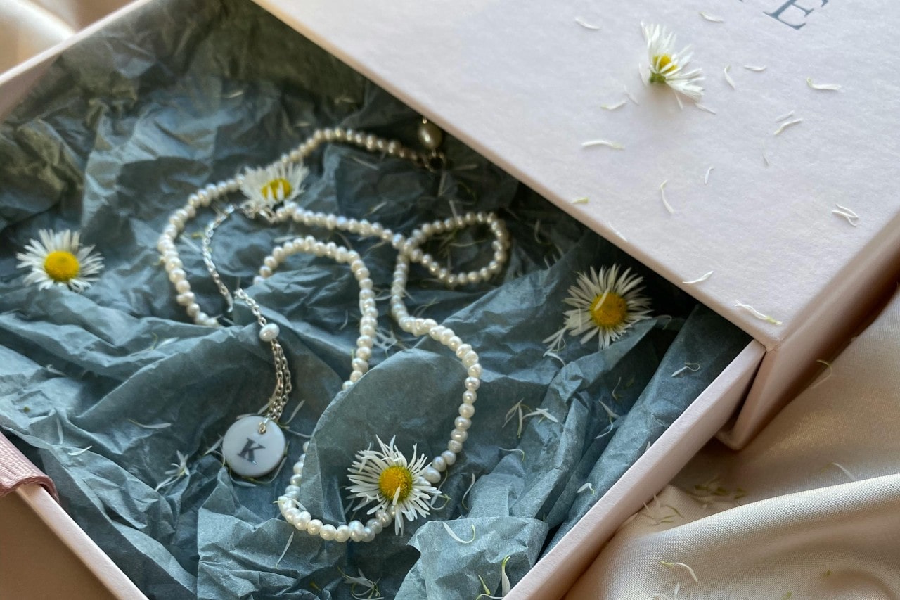 a long pearl necklace with an initial pendant in a gift box with flowers and tissue paper