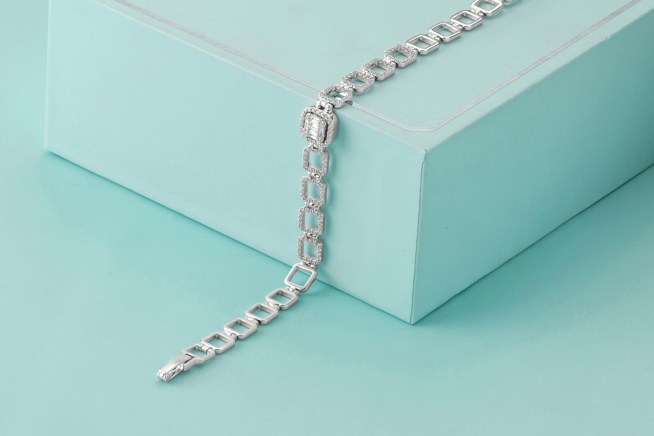 a white gold chain bracelet with diamond accents lying across a light blue box