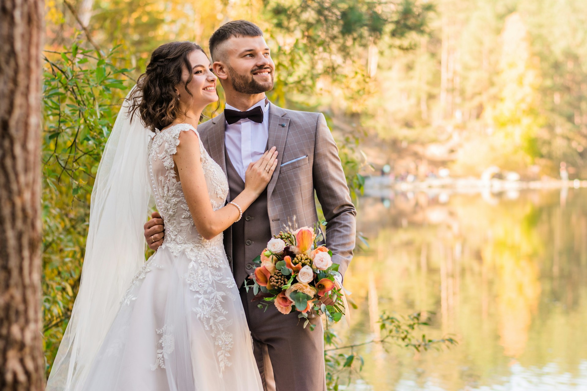 a bride and groom standing by a lake