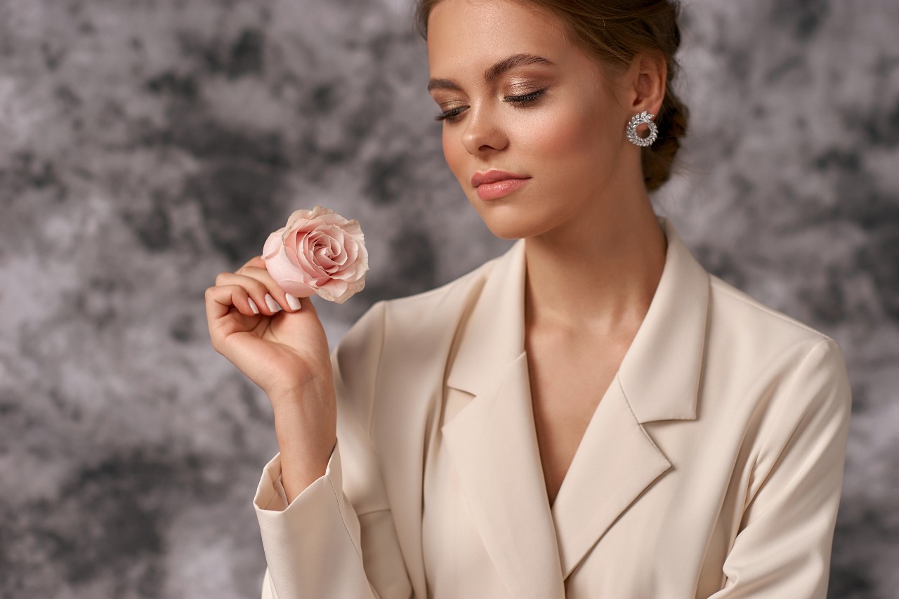 a business woman holds a flower while wearing circle diamond earrings.