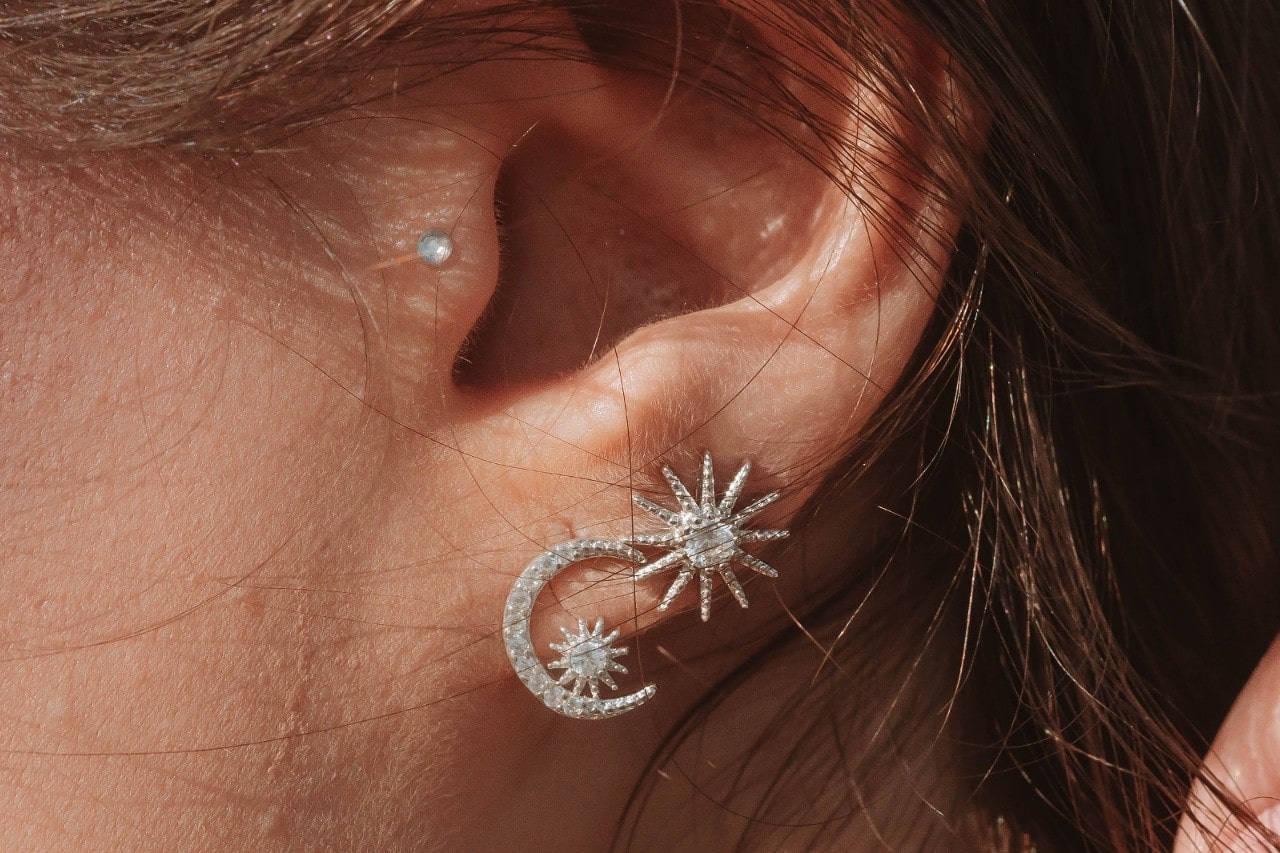 A woman’s ear with multiple piercings wearing celestial diamond earrings.