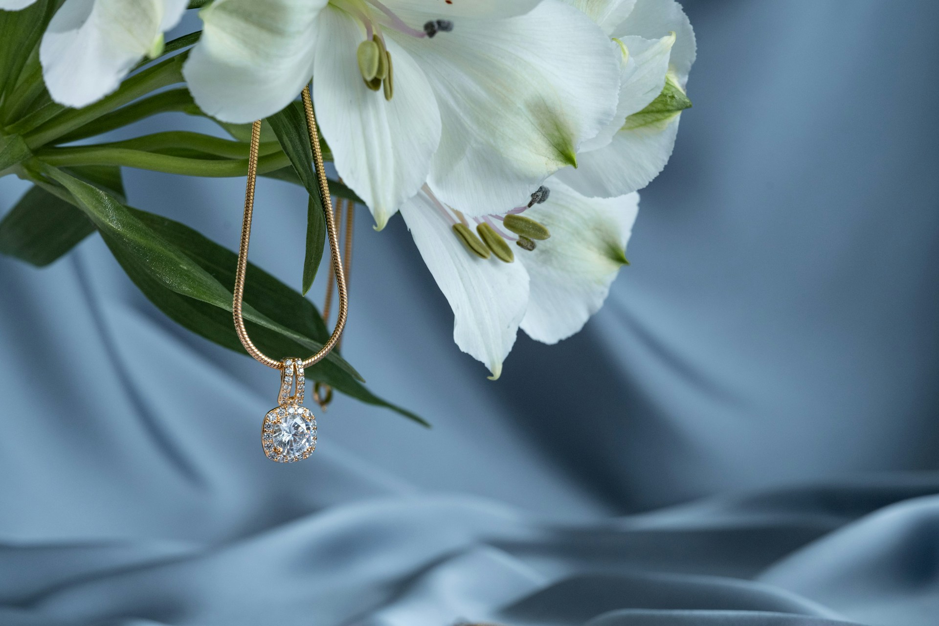 a yellow gold diamond pendant necklace hanging off of a bouquet of flowers