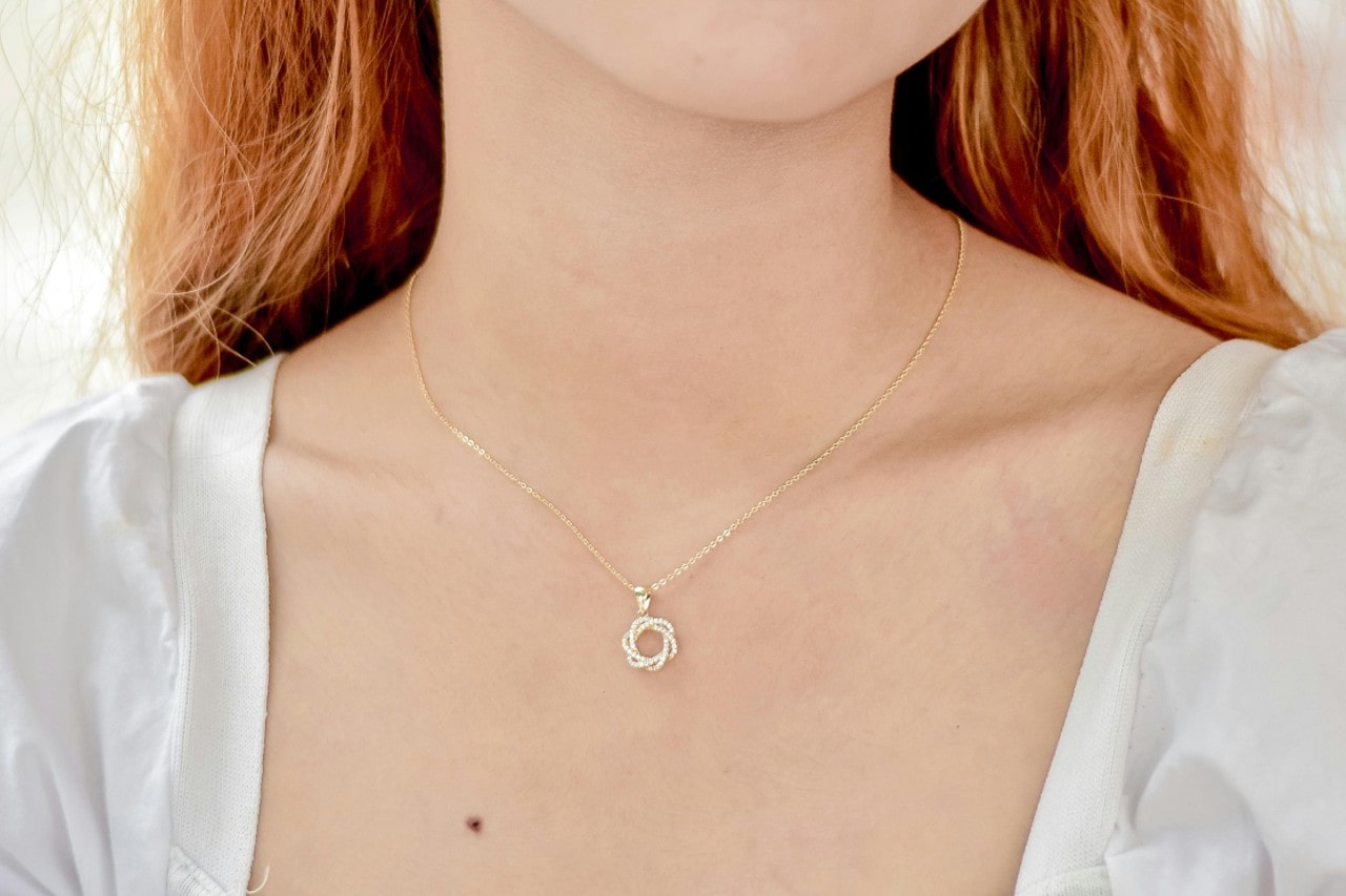 close up image of a woman’s neckline adorned with a yellow gold diamond pendant