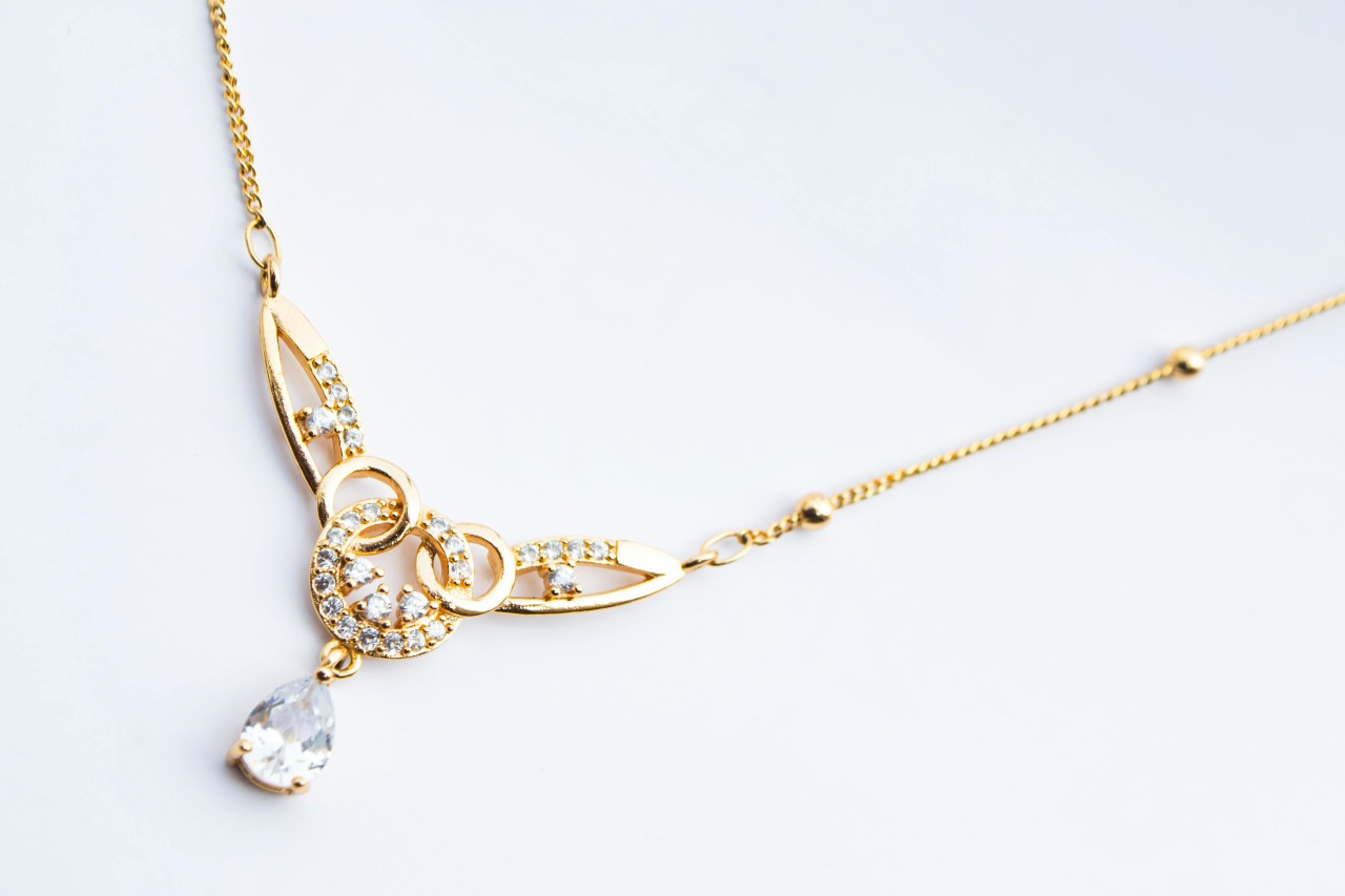 close up image of a yellow gold necklace with a pear shape diamond and intricate details