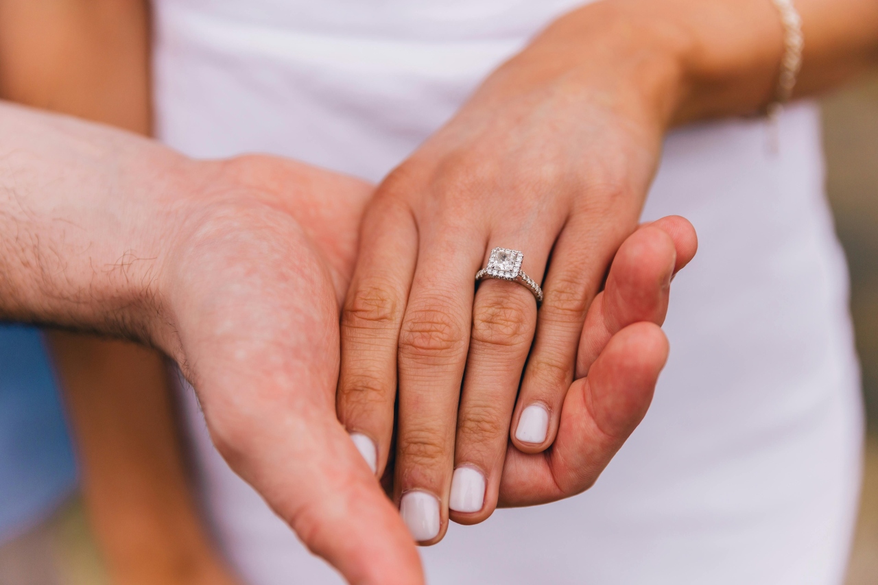 A close-up of a bride-to-be’s hand in her groom’s, with emphasis on her princess-cut engagement ring.