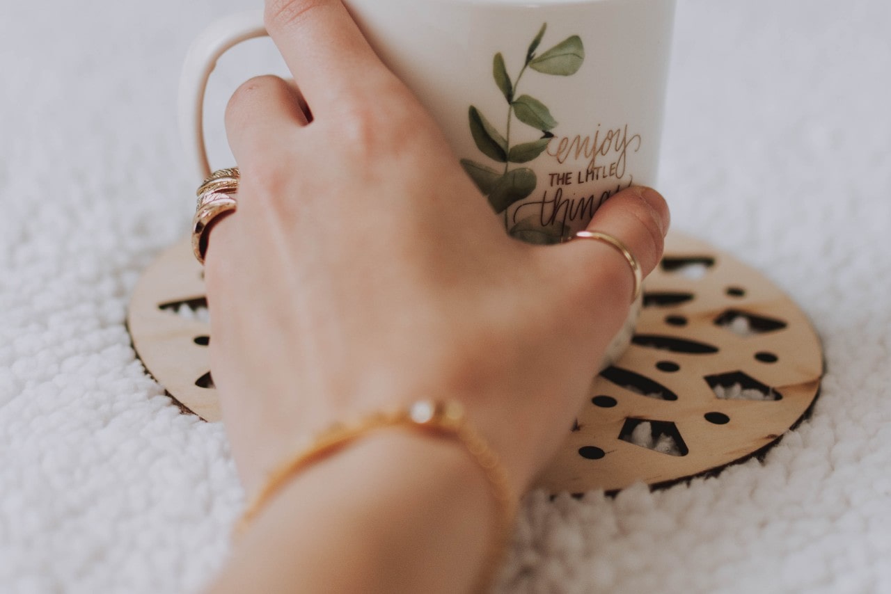 A close-up of a woman’s hand adorned in beautiful gold jewelry, holding a charming mug.