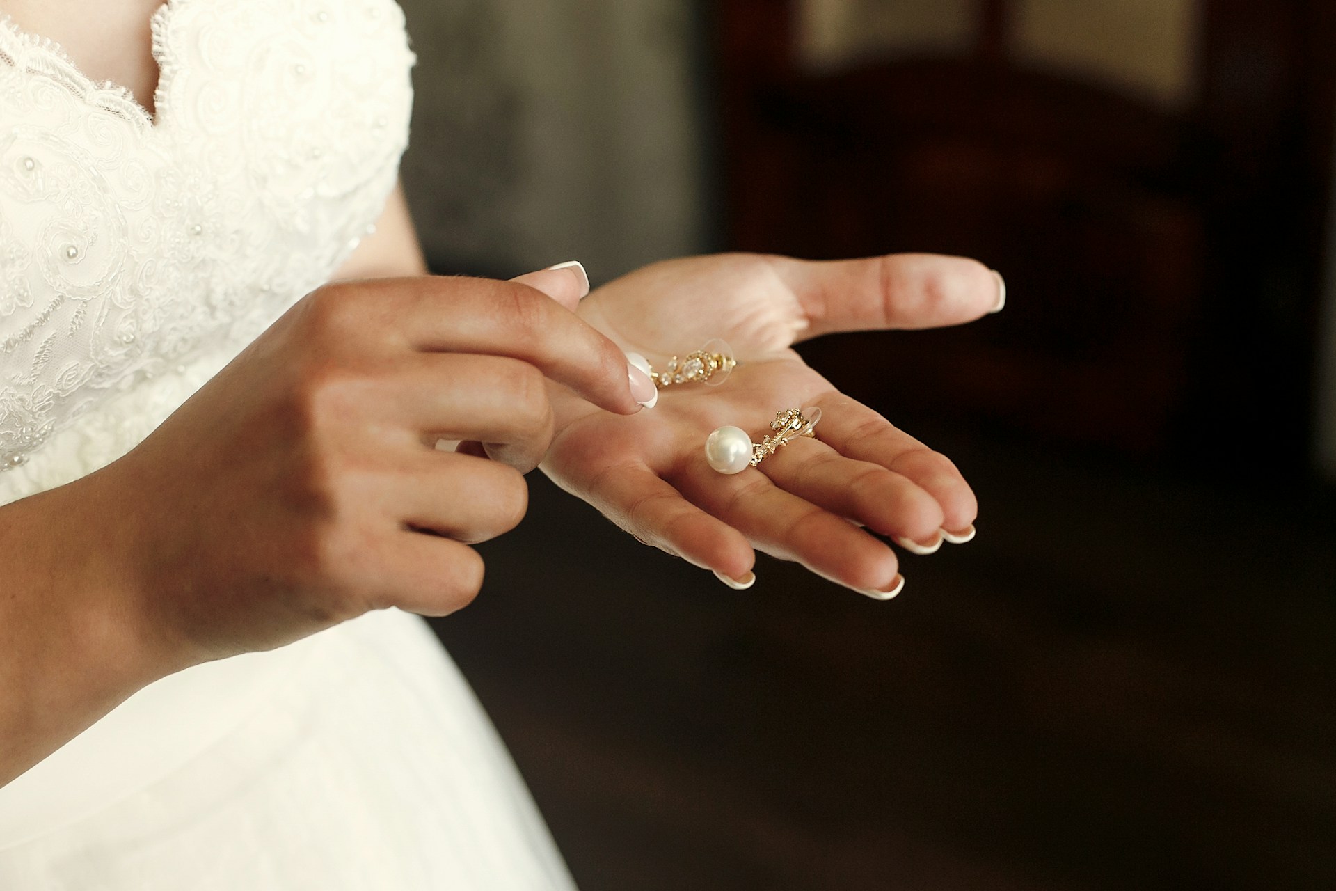 A close-up of a bride-to-be holding a pair of pearl earrings in her palm.